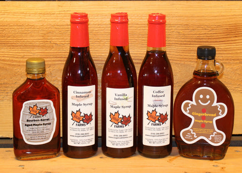 Five bottles of infused maple syrup with different flavors on a wooden surface.