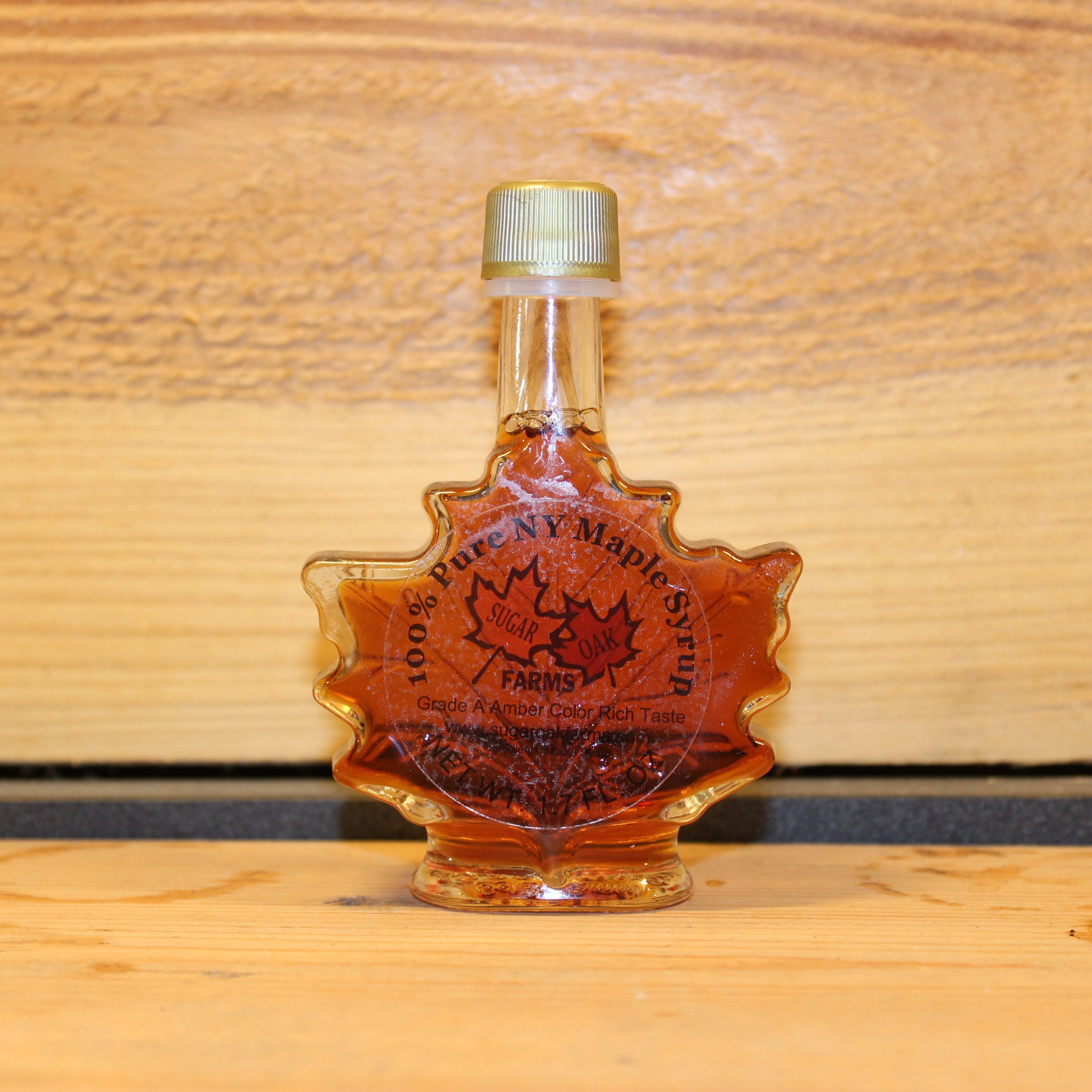 Bottle of 1.7 fluid ounces of maple syrup with a visible Sugar Oaks Farm brand logo on a wooden surface.